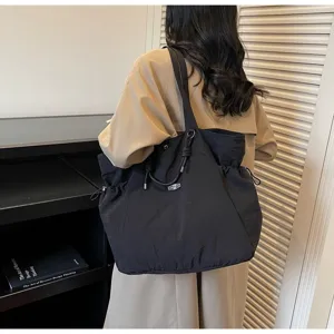 Back view of a black waterproof large capacity shoulder travel tote bag worn with a trench coat