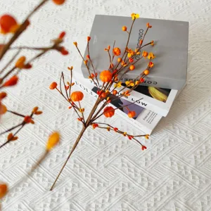 Detailed view of artificial orange pumpkin berry branch on books for harvest decor