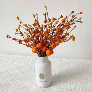 Detailed view of artificial orange berry stems with mini pumpkins in a white vase.