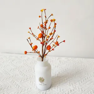 Close-up of orange artificial berry and pumpkin branch in white vase for home decor
