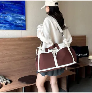 Model carrying a large brown and white duffel bag in a modern cafe setting.