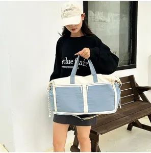 Large blue and beige travel duffel bag held by a model in a lifestyle setting.