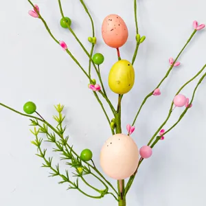 Osterzweig Detailansicht mit bunten Ostereiern, grunen Beeren und rosa Bluten als Dekoration.