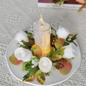 Detailed view of LED candle with white rose floral wreath and autumn leaves for wedding decor.