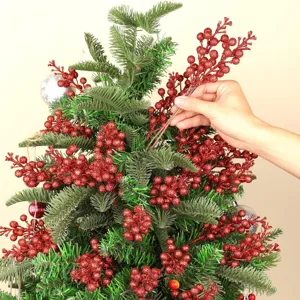 Nahaufnahme von roten Glitzer-Beerenstielen am grünen Weihnachtsbaum für die Deko.