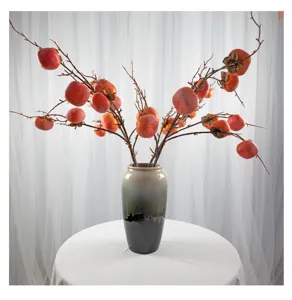 Composizione floreale di rami di cachi artificiali in vaso di ceramica per decorazione.