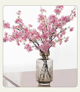 Close up detail of artificial pink cherry blossom branches in a textured glass vase decor.