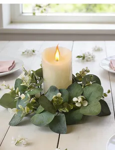 Detailed view of a green eucalyptus candle ring with a warm flame on a white table.