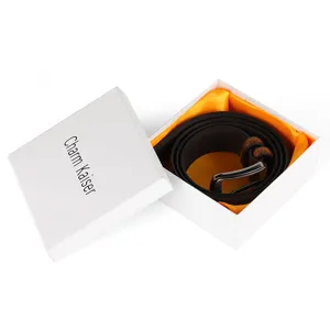 Detailed view of brown leather belt inside a premium white gift box with orange lining