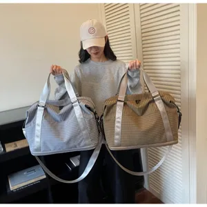 Close-up of two large quilted travel bags in gray and khaki colors held by a female model