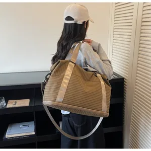 Side detail of a large brown checkered travel bag carried by a person in a minimalist room