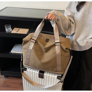 Large brown checkered travel duffel bag with shoulder strap on a white suitcase