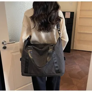 Large capacity checkered travel bag with shoulder strap worn by a woman in a stylish room