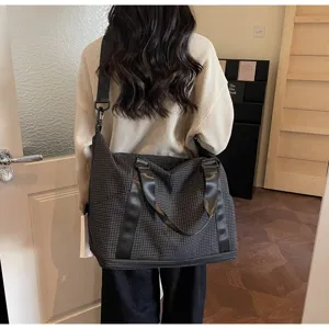 Large capacity grid pattern travel bag worn by a model in a modern lifestyle indoor setting