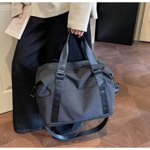Detail view of a large grey grid pattern travel bag held by a model in a stylish indoor setting