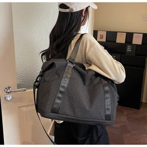 Woman carrying a large black grid travel bag in a lifestyle indoor setting