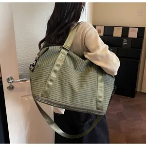 Large capacity green checkered travel bag shown on model in a cozy indoor room setting