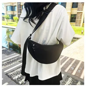 Detail of a minimalist black crescent crossbody bag worn outdoors on a white T-shirt.