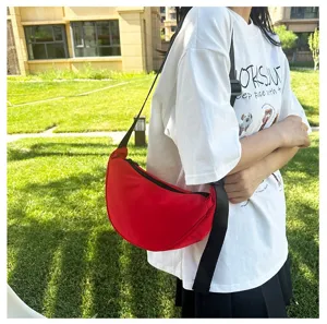 Red crescent crossbody bag styled with a casual outfit in an outdoor park setting.