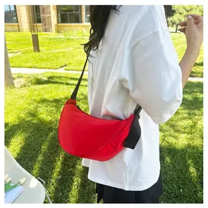 Detail of red crescent crossbody bag worn by a model in a sunny outdoor park setting