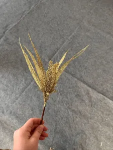 Detalle de una rama de helecho artificial con purpurina dorada para decorar el árbol