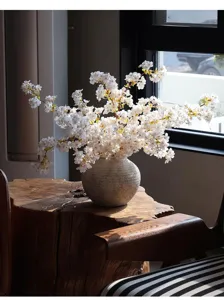 Vista detallada de ramas de cerezo artificiales blancas en un jarrón de cerámica rugoso