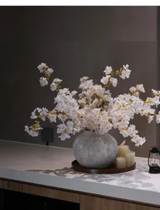 Primer plano de elegantes ramas de cerezo artificiales en un jarrón de piedra rústico