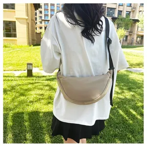 Back view of a minimalist beige dumpling crossbody bag styled with a casual outfit outdoors