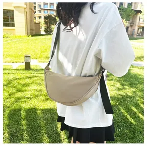 Lightweight minimalist beige crescent crossbody bag shown in a casual outdoor lifestyle setting