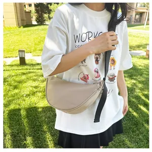 Model wearing a minimalist beige crescent crossbody bag in an outdoor park setting