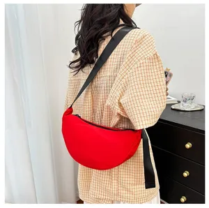 Model wearing a red crescent-shaped crossbody bag with adjustable black strap