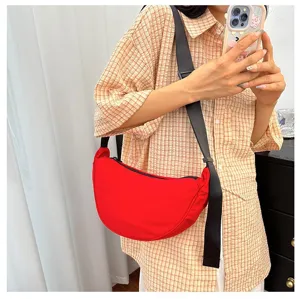 Vibrant red crescent dumpling bag worn as a crossbody with a black adjustable strap