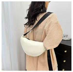Detail view of a cream minimalist crescent crossbody bag worn with a black strap