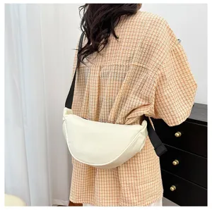 Detail view of a minimalist cream dumpling crossbody bag worn by a model in a plaid shirt