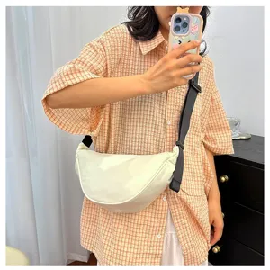 Model wearing a minimalist cream-colored dumpling crossbody bag with an adjustable strap.