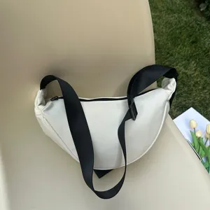 A minimalist white crescent dumpling crossbody bag with an adjustable black strap