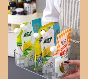 Clear multi-compartment storage box organizing various seasoning pouches in a kitchen.