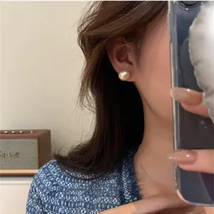 Elegant large pearl stud earrings worn by a model shown in a mirror selfie perspective