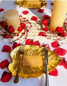 Romantic tabletop setup with red heart berry candle wreaths and rose petals.