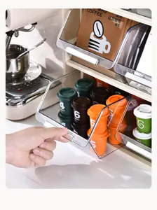 Close-up of a hand opening the transparent drawer of a coffee capsule organizer rack.
