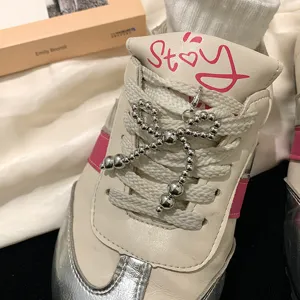 Close-up of a silver beaded bow shoe charm attached to white sneaker laces on a book.