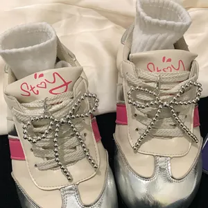 Detailed view of shiny silver beaded bow shoe charms attached to white athletic sneakers