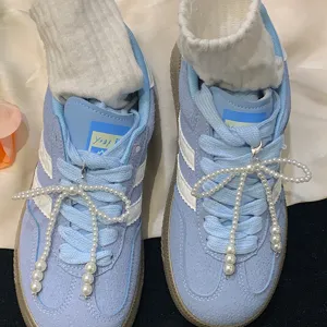 Close-up view showing elegant white pearl bow charms decorating light blue suede sneakers.