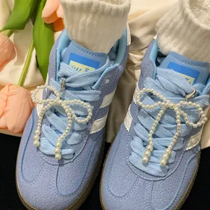 Macro detail shot of white pearl bow charms attached to blue suede sports sneakers