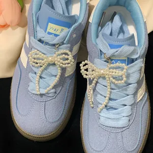 Close-up detail showing elegant white pearl bow shoe charms on light blue sneakers.