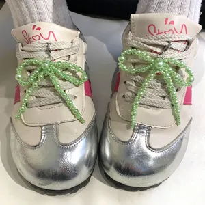 Détail de breloques de chaussures en perles vertes sur des baskets beiges décor