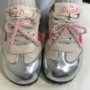 Gros plan de breloques de chaussures en perles roses fixées aux lacets de baskets