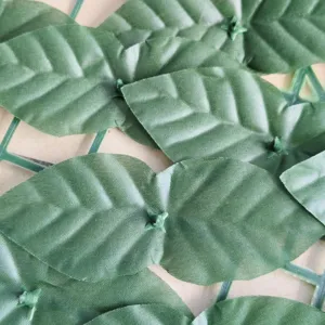 Makro-Detail von künstlichen grünen Heckenblättern auf einem Kunststoff-Zaungitter