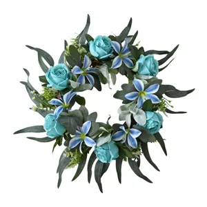 Macro view of blue artificial roses and lilies in a lush green leaf floral wreath.