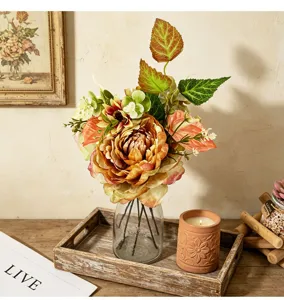 Dettaglio di un bouquet di peonie e crisantemi artificiali in un vaso su un vassoio rustico.